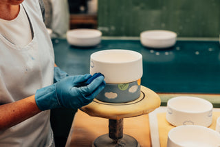 A ceramicist hand-painting blue dots onto stoneware plates at the Egg Back Home workshop